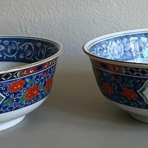May include: Two round porcelain bowls featuring a white interior and a decorative exterior band. The exterior displays a pattern of vibrant orange flowers, green leaves, and blue geometric accents against a white and blue floral background.