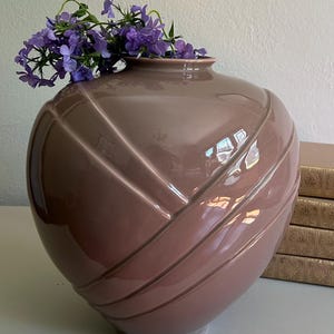 May include: A mauve-colored ceramic vase with a glossy finish, featuring a diagonal ribbed design. The vase is filled with vibrant purple flowers. Decorative home decor item.