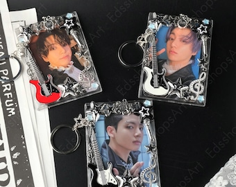 May include: Three clear acrylic keychains featuring a photo of a person, a guitar, and star-shaped accents. The guitar on each keychain is a different color: red, white, and black. Each keychain has a silver-colored border with star and musical note details.