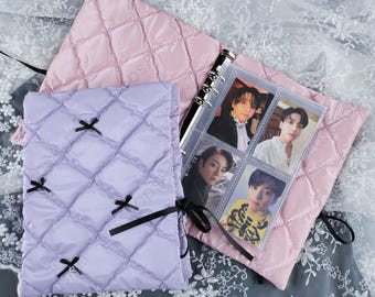 May include: A light purple quilted binder cover with black bow accents and a pink quilted binder cover. The binder contains photo cards. The covers are on a white lace background.