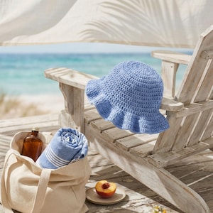 May include: A light blue crochet sun hat with a ruffled brim rests on a wooden Adirondack chair. A canvas tote bag holds a rolled blue and white striped towel and a brown bottle. A peach sits on a small plate, with the ocean in the background.