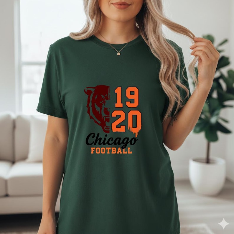May include: Dark green t-shirt featuring a Chicago Bears design. The design includes a bear head graphic, the numbers "19 20", and the words "Chicago FOOTBALL" in orange and black. The shirt is short-sleeved.