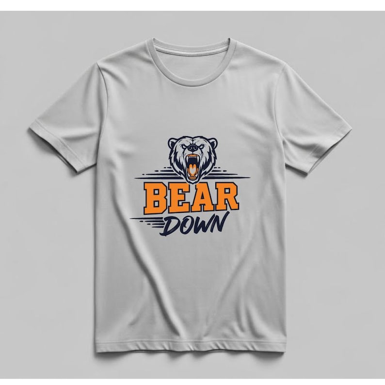 May include: A light gray t-shirt featuring a graphic of a bear's head with an open mouth and the words "BEAR DOWN" in orange and navy blue. The bear graphic is above the text.