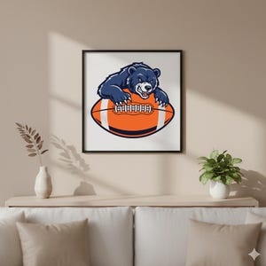 May include: A framed print featuring a navy blue bear with a fierce expression, perched atop an orange and white football. The artwork is set against a white background, framed in black, and suitable for sports enthusiasts.