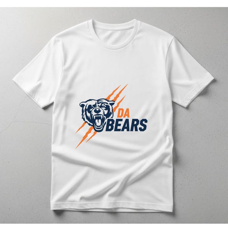 May include: White t-shirt featuring a navy blue bear graphic with the text "DA BEARS" in navy blue and white. The design includes orange claw marks. A classic crew neck tee.