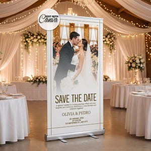 May include: A wedding reception venue with round tables covered in white tablecloths. A large banner displays a couple kissing with the text "Save the Date". The banner is in front of the tables. Floral arrangements and string lights decorate the room.
