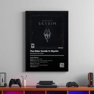 以下が含まれることがあります： 「The Elder Scrolls V: Skyrim」のビデオゲームの白黒フレームポスター。ポスターには、ゲームのロゴと詳細（ゲームプロファイル、リリース日、プラットフォーム、ジャンルなど）が表示されています。ポスターは木製のコンソールの上に表示されています。