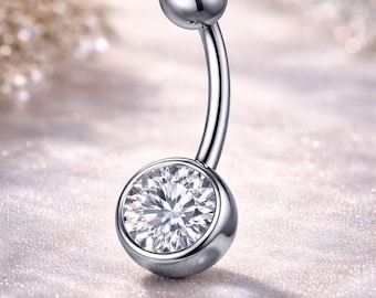 May include: A curved belly button ring with a polished silver finish. The jewelry features two round, clear gemstones, one at the top and a larger one at the bottom. The gemstones sparkle against a soft, blurred background.