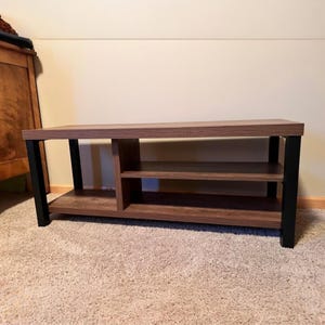 May include: A rectangular, brown wooden coffee table with black metal legs. The table has two shelves and a side compartment for storage. The table is approximately 48 inches long, 16 inches high, and 20 inches wide.