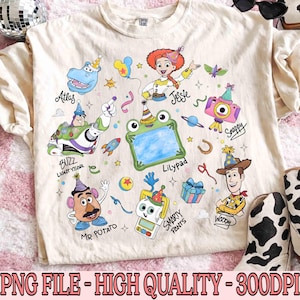 May include: Cream-colored t-shirt featuring colorful cartoon characters including Buzz Lightyear, Jessie, and Woody. The shirt has the text "Atlas", "Jessie", "Buzz Lightyear", "Lilypad", "Mr. Potato", "Snappy", "Smarty Pants", and "Woody".