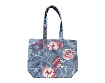 May include: A tote bag with a floral pattern in shades of blue, red, and pink. The bag has a rectangular shape with a small pocket on the front and two handles. The floral design includes large blooms and foliage.
