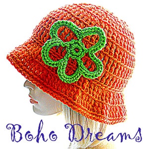Pode incluir: Um chapéu de sol de crochê na cor laranja com um design de flor verde. O chapéu se chama "Boho Dreams" e é de Elvee Dickinson.