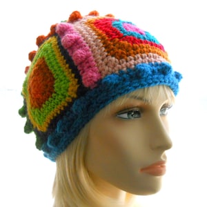 May include: A colorful crocheted hat with a geometric pattern in shades of orange, green, pink, red, and blue. The hat has a textured, bumpy design.