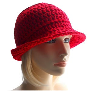 May include: A red crocheted hat with a wide brim. The hat is worn by a mannequin with blonde hair.