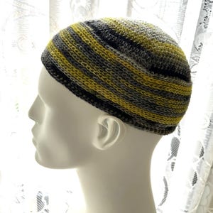 May include: A crochet beanie cap featuring horizontal stripes in shades of charcoal gray, light gray, and vibrant yellow. The knit pattern is consistent throughout the rounded crown and the folded brim, showcasing a textured yarn construction.
