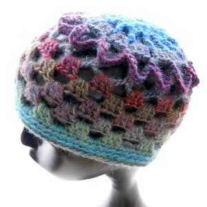 Pode incluir: Um chapéu de crochê colorido com um design de renda. O chapéu é feito com uma variedade de tons de azul, verde, roxo e vermelho.