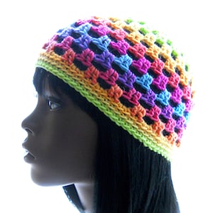Puede incluir: Un gorro de punto de ganchillo colorido con un patrón de arcoíris. El gorro está hecho con una variedad de colores brillantes, incluyendo rosa, naranja, amarillo, verde, azul y morado.