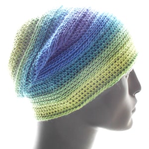 May include: A crocheted beanie hat with a gradient of green, blue and purple colours. The hat is made with a textured stitch and has a slouchy fit.