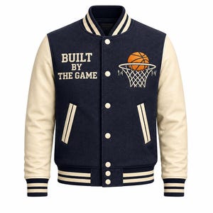 Op de afbeelding: Marineblauwe en crèmekleurige varsity-jas met een basketbal- en hoepelafbeelding. De jas heeft de tekst "BUILT BY THE GAME" en heeft crèmekleurige mouwen en gestreepte manchetten. Een klassieke jas met sportthema.