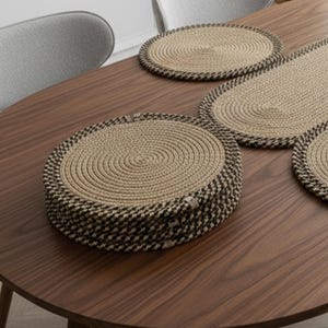 Peut inclure: Ensemble de sets de table et chemin de table tissés beiges naturels, bordés d'un motif à carreaux marron foncé et blanc. Les sets de table sont ronds et ovales, disposés sur une table en bois brun foncé.