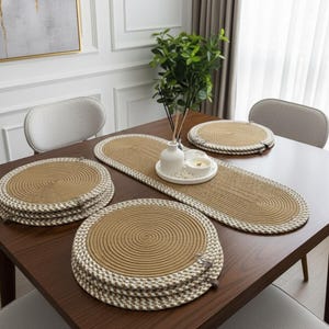 Peut inclure: Ensemble de sets de table et chemin de table tressés. Les sets de table ronds et le chemin de table ovale ont un centre marron clair et une bordure crème. Un vase de verdure est posé sur la table en bois foncé.