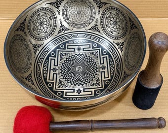 以下が含まれることがあります： 複雑な黒の幾何学模様と中央にオームのシンボルが描かれた銀色の金属製シンギングボウル。セットには、黒いフェルトベースの木製マレットと、大きな赤いフェルトボールが付いた木製のスティックが含まれています。
