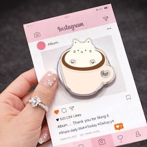Może przedstawiać: Różowy notatnik w stylu Instagrama z kotem w filiżance kawy. Notatnik ma interfejs mediów społecznościowych ze słowem "Instagram" u góry i wzorem filiżanki kawy w kształcie serca. Notatnik zawiera również tekst "Album... Dziękuję za polubienie."