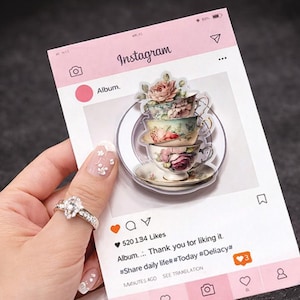 Op de afbeelding: Een roze Instagram-kaart met een stapel vintage theekopjes. De theekopjes hebben bloemmotieven. De kaart toont het Instagram-logo, een hartpictogram en de tekst "Album... Thank you for liking it." De kopjes staan op een heldere, cirkelvormige basis.