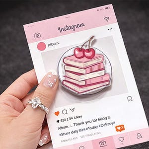 Op de afbeelding: Een roze Instagram-thema notitieblok met een stapel roze boeken met kersen. Het notitieblok heeft een social media interface ontwerp met het woord "Instagram" bovenaan en een like-aantal van 520.134.
