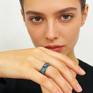 May include: A silver ring with a colourful enamel design. The ring features a pattern of blue, green, and white enamel. The ring is worn on a finger.