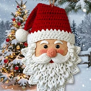 Puede incluir: Adorno navideño de Papá Noel hecho a mano con ganchillo. El adorno presenta un gorro rojo con ribete blanco, una nariz color melocotón y una barba blanca. El fondo incluye un árbol de Navidad nevado y una escena invernal.