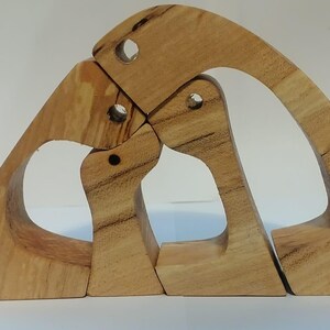 Puede incluir: Un conjunto de tres esculturas de madera entrelazadas hechas de madera de color claro con patrones de grano natural visibles. Las piezas tienen formas curvas y arqueadas con pequeños recortes circulares, encajando entre sí para crear una unidad cohesiva.
