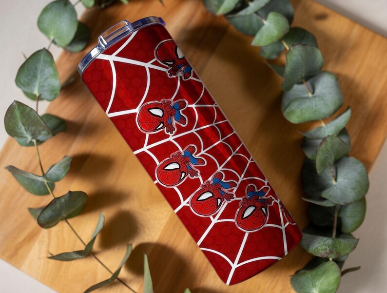 Może przedstawiać: Czerwono-biały kubek z motywem Spider-Mana. Kubek ma czerwone tło z białym wzorem pajęczyny i kilkoma grafikami twarzy Spider-Mana. Cylindryczny kubek ma srebrną pokrywę.