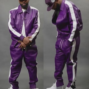 May include: A two-piece purple tracksuit with white stripes down the sides. The jacket has a button-up front and the pants have a drawstring waist. The outfit is paired with a matching baseball cap and white sneakers.