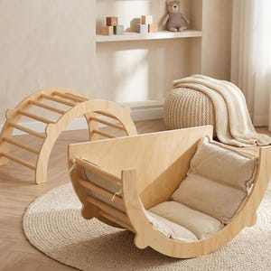 Puede incluir: Juego de arco de escalada y balancín de madera. El arco tiene barras de madera para escalar. El balancín tiene un asiento acolchado. El juego está hecho de madera de color claro y está diseñado para el juego de los niños. Una alfombra redonda está debajo del balancín.