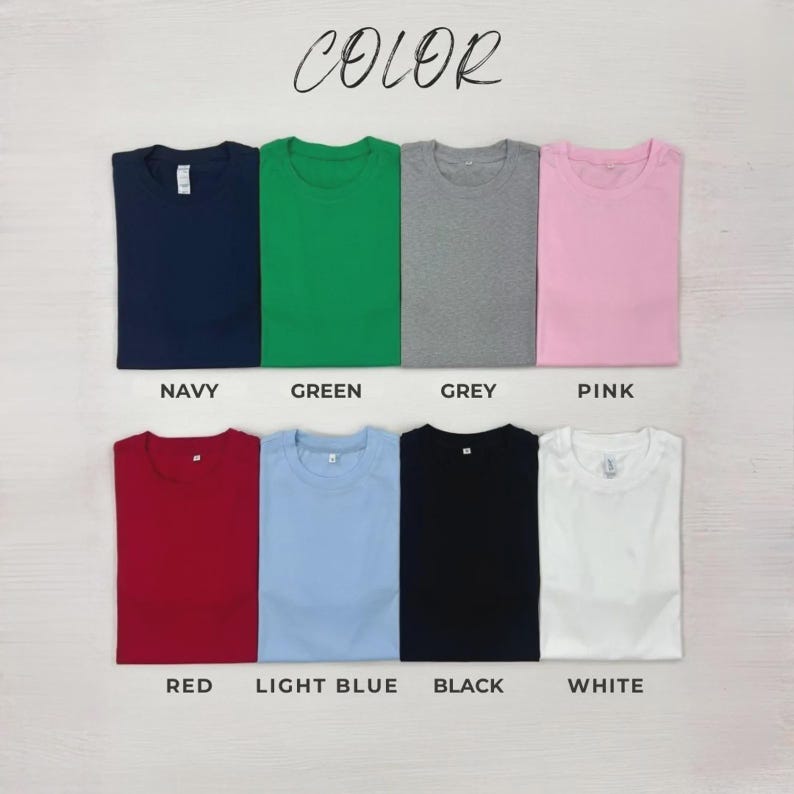 May include: A collection of eight short-sleeved crew neck t-shirts arranged in two rows. The colours include navy, green, grey, pink, red, light blue, black, and white. Each shirt is labelled with its corresponding colour name printed below it.