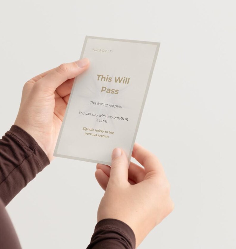 May include: A rectangular card with the text "This Will Pass" in a soft, neutral font. The card also includes the phrases "This feeling will pass," "You can stay with one breath at a time," and "Signals safety to the nervous system."
