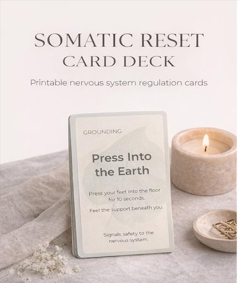 May include: A card deck titled "SOMATIC RESET CARD DECK" with the text "Printable nervous system regulation cards." One card reads "Press Into the Earth." A lit candle and small dish with paper clips are also visible.