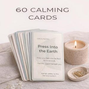 May include: A stack of 60 calming cards with the text "Press Into the Earth" and instructions. A lit candle and a small dish with paper clips are next to the cards. The text "60 CALMING CARDS" is at the top.