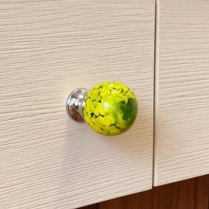 May include: A close-up of a wooden cabinet with drawers. One drawer is open, revealing a light wood interior. The drawer front is off-white with a yellow and green knob. The cabinet has a dark wood top and sides.