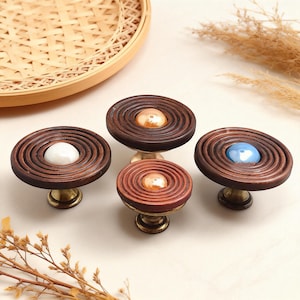 May include: Four decorative cabinet knobs with a spiral design. The knobs have a dark brown wooden finish with a central accent in white, gold, copper, and blue. Each knob is mounted on a brass base, offering a vintage aesthetic.