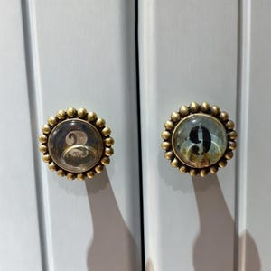 May include: A set of three ceramic mugs with a speckled, cream-colored glaze. Each mug features a different hand-painted floral design in shades of blue, green, and yellow. The mugs have a simple, rounded shape and a comfortable handle.