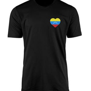 May include: Black crew neck t-shirt with a heart-shaped Venezuelan flag design on the left chest. The flag design features yellow, blue, red, and white colours. The shirt is made of a soft, comfortable material.