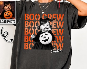 May include: A charcoal gray short-sleeve t-shirt featuring a graphic print of a child in a black dress holding a pumpkin bucket. The text BOO CREW is repeated in orange behind the child, and the name Sophia is printed in white script below.