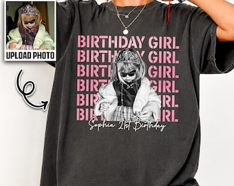 May include: A charcoal gray short-sleeve t-shirt featuring a graphic print of a person wearing a tiara and sunglasses. The text "BIRTHDAY GIRL" is repeated in pink, with the name "Sophia" and "21st Birthday" printed in white script below.