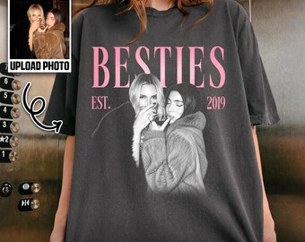 May include: A charcoal gray short-sleeve t-shirt featuring a custom black and white photograph of two people. The text BESTIES is printed in large pink letters above the photo, with EST. 2019 on the sides. The words CUSTOM PHOTO appear below.