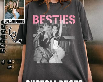 May include: A charcoal gray short-sleeve t-shirt featuring a black and white photographic print of two individuals with the pink text BESTIES above the image and the white text CUSTOM PHOTO printed at the bottom of the garment.