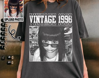 May include: A charcoal gray short-sleeve t-shirt featuring a graphic print with the text VINTAGE 1996. The design includes a black and white photographic image of a person with dark hair wearing sunglasses, layered over a comic book style background.