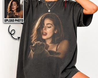 May include: Dark gray t-shirt featuring a photographic print of a woman holding a cat. The shirt has a vintage, washed-out look. The words "UPLOAD PHOTO" are printed on a small image on the left side of the shirt, and the word "PEPPER" is printed on the upper right.