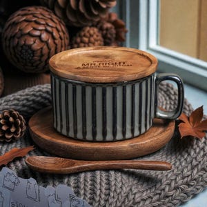 May include: A ceramic mug with vertical black stripes, a wooden lid, and a matching saucer. The lid is engraved with the words "MR. RIGHT A SENSE OF RITUAL". A small wooden spoon rests on a gray knitted surface.